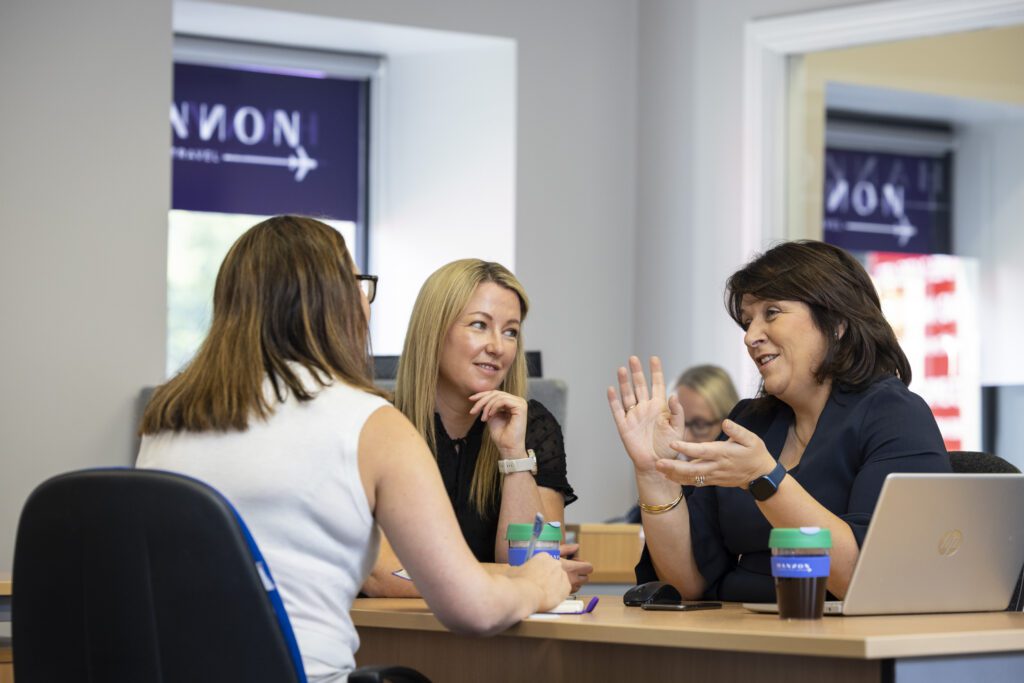 Three women sit around desk discussing work